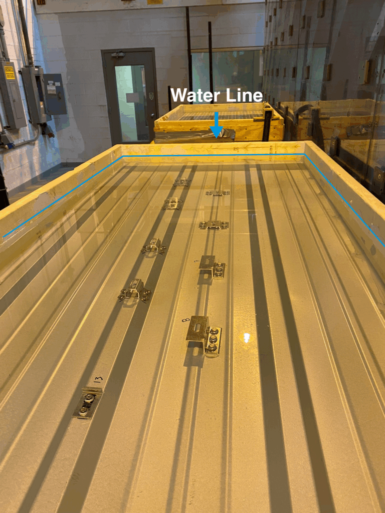 Water line visible on a large table, with S-5! brackets installed on a sample metal roof material submerged in water.