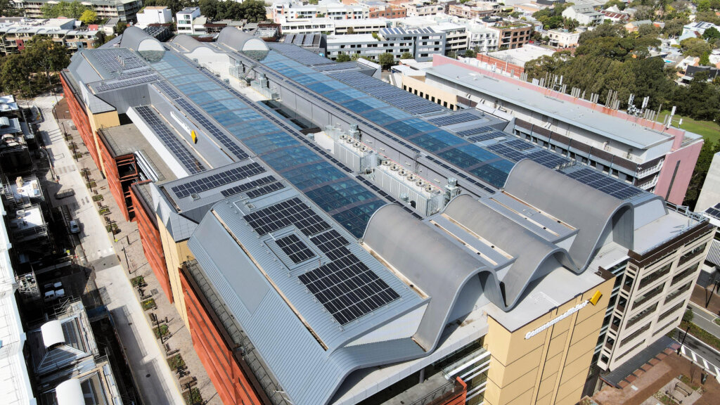 Aerial view of a building with solar panels, glass skylights, and curved grey metal roof sections.